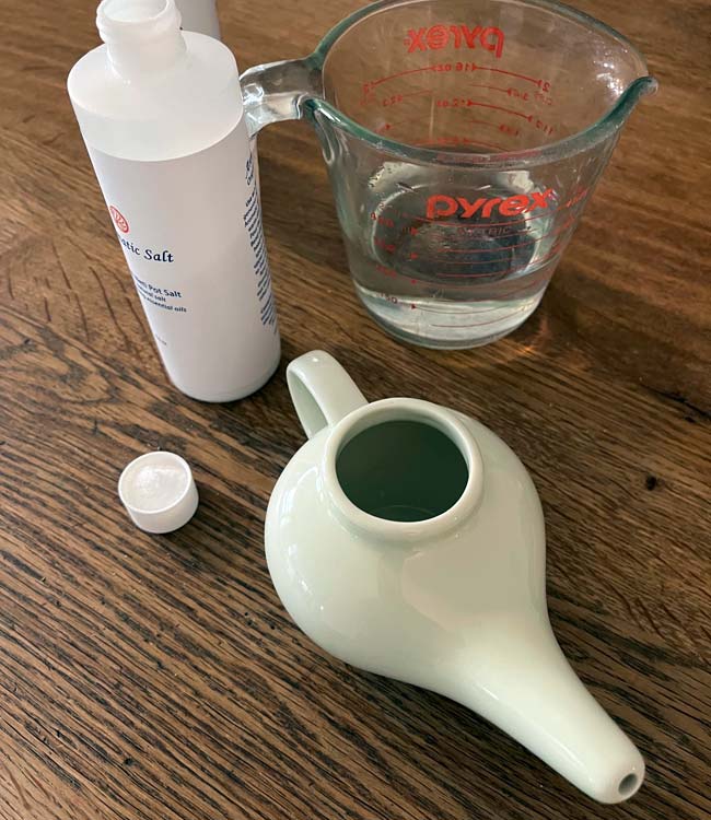 Distilled Heated Water in a Measuring Cup, Aromatic Salt, Neti Pot and Cap on a Wood Table