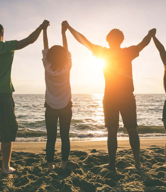 People Holding Raised Hands on the Beach With the Sunset in Front of Them