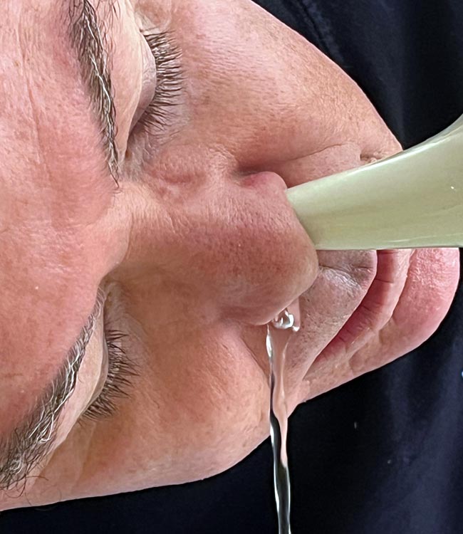 Man Using a Neti Pot With Solution Flowing From One Nostril and out the Other