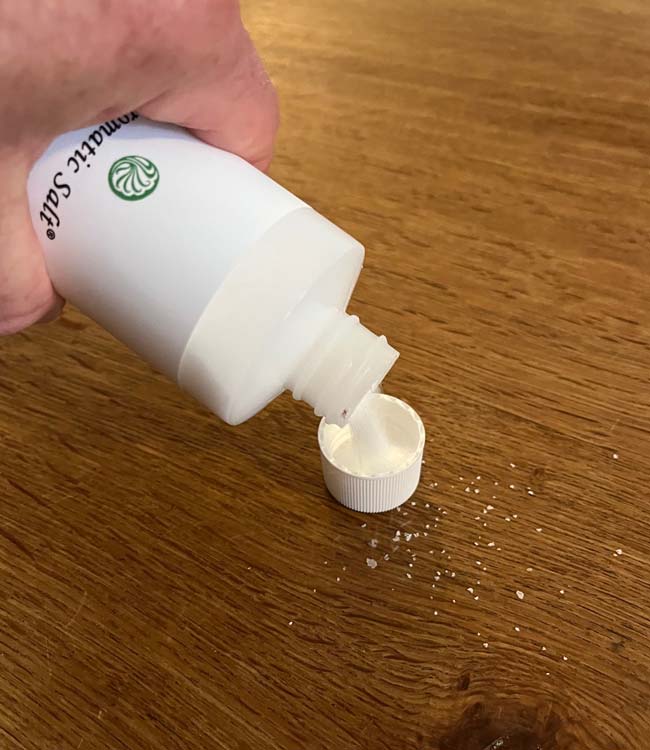 Person Pouring Neti Pot Solution Salt Into a Cap On a Wooden Tabletop